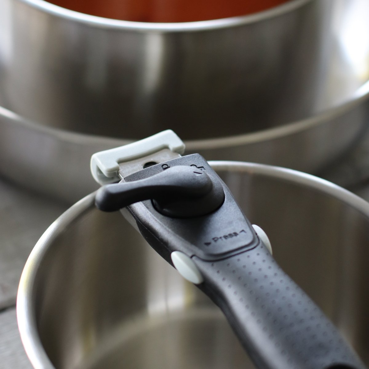 Gros plan poignée amovible noire clipsée sur casserole inox, système de fixation détaillé