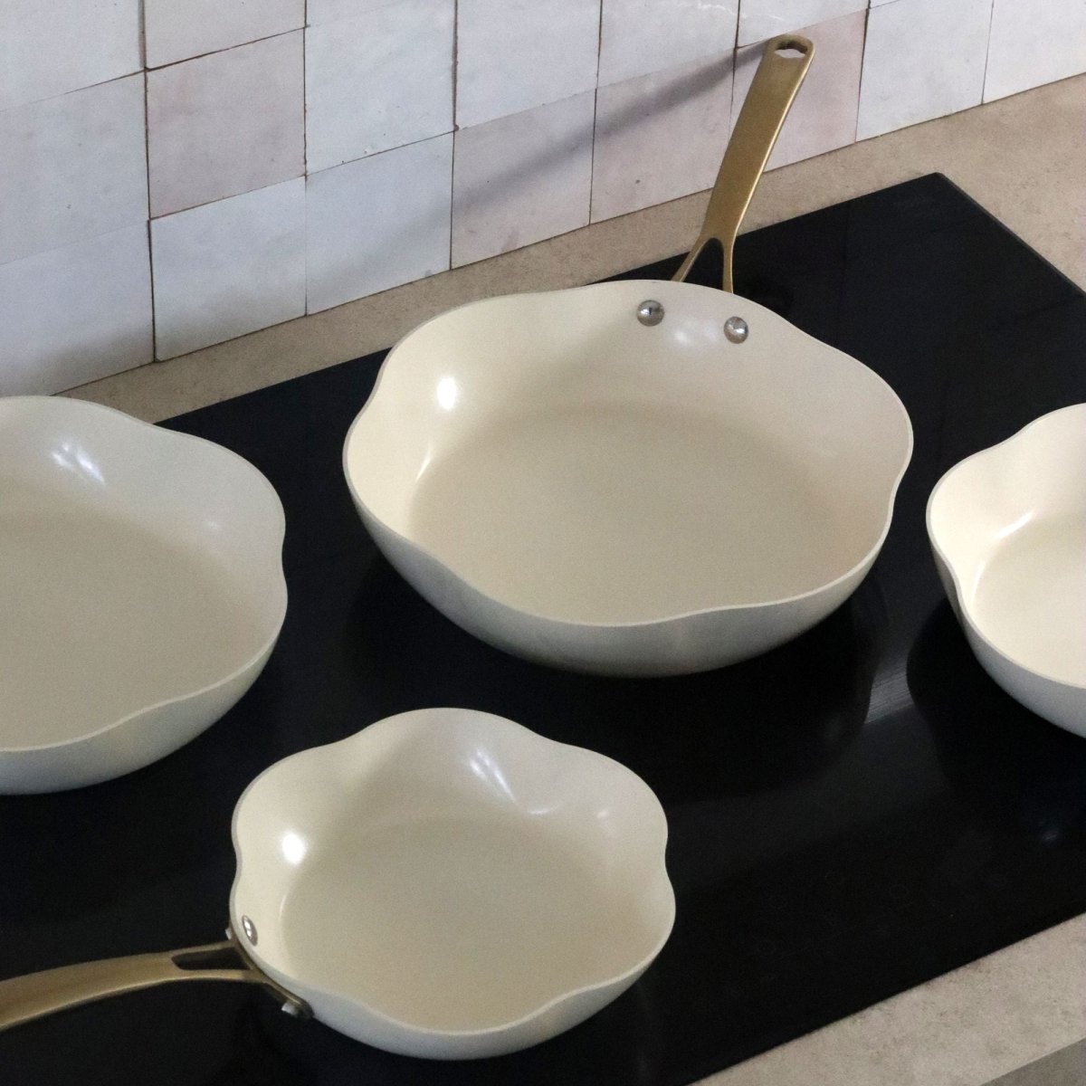 Set de 3 poêles Dahlia en aluminium recyclé beige, vue d'ensemble sur plan de travail noir avec carrelage blanc