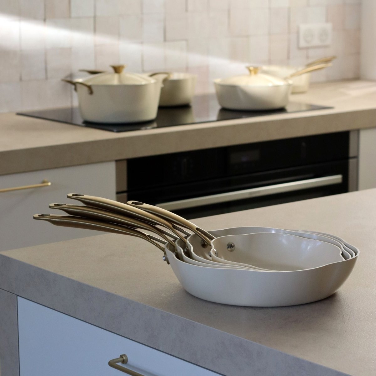 Set de 3 poêles Dahlia en aluminium recyclé beige empilées sur plan de travail, cuisine moderne avec casseroles en arrière-plan