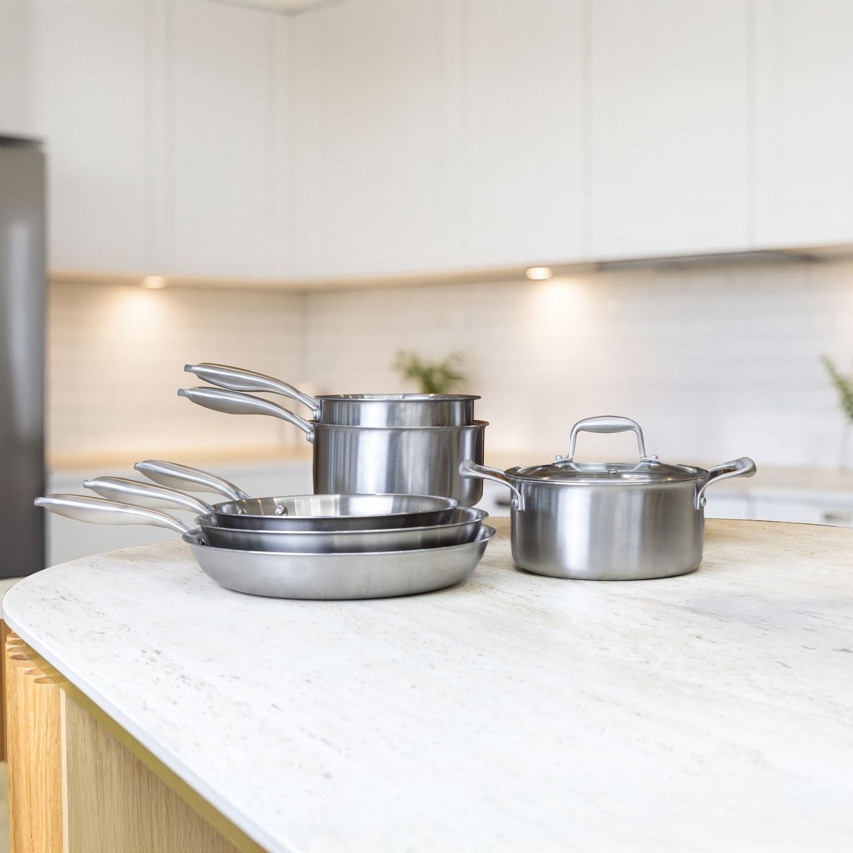 Set de 3 poêles Trinox et casseroles en acier inoxydable posé sur îlot de cuisine moderne avec plan de travail blanc