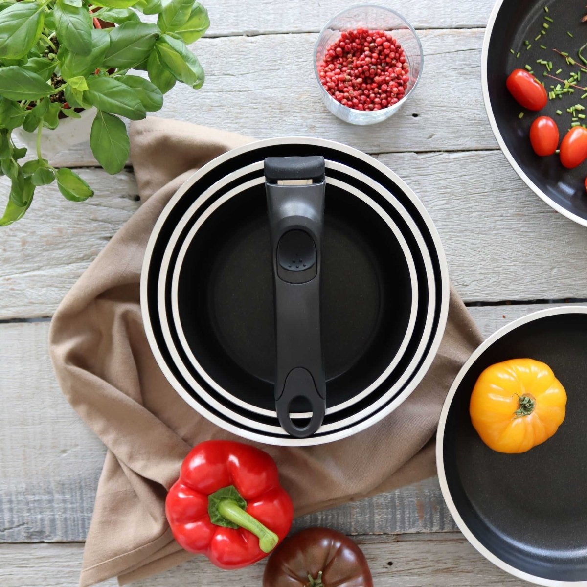 Vue de dessus du set 4 pièces batterie de cuisine en aluminium noir avec poignée amovible, entouré de légumes frais sur table en bois