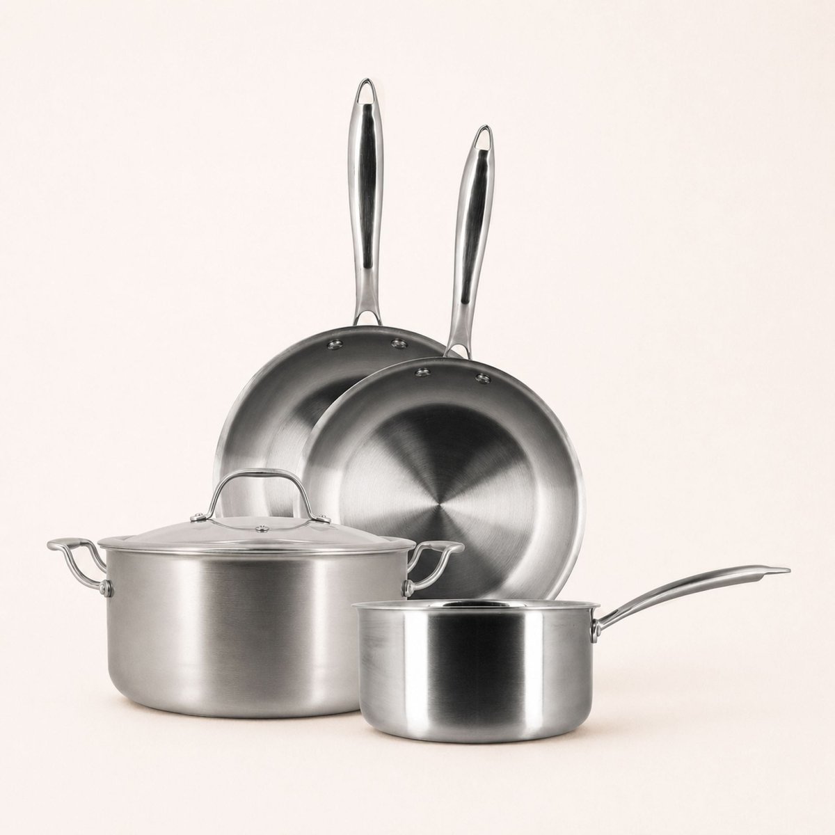 Set de 4 pièces Triply Menastyl en acier inoxydable : 2 poêles, 1 casserole et 1 faitout avec couvercle sur fond beige