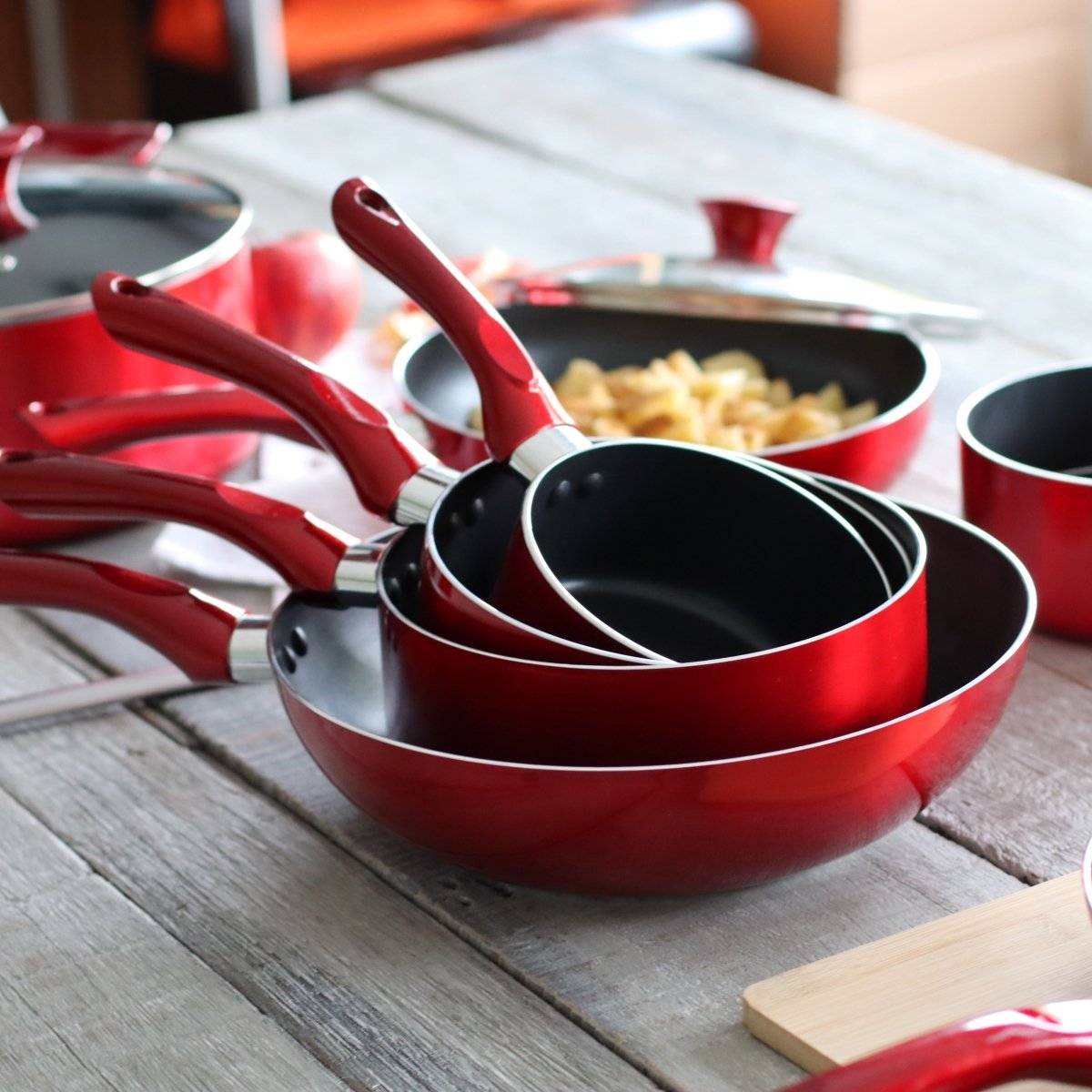 Set de 5 pièces de cuisine rouge cerise en aluminium avec revêtement antiadhésif noir, disposées sur table en bois