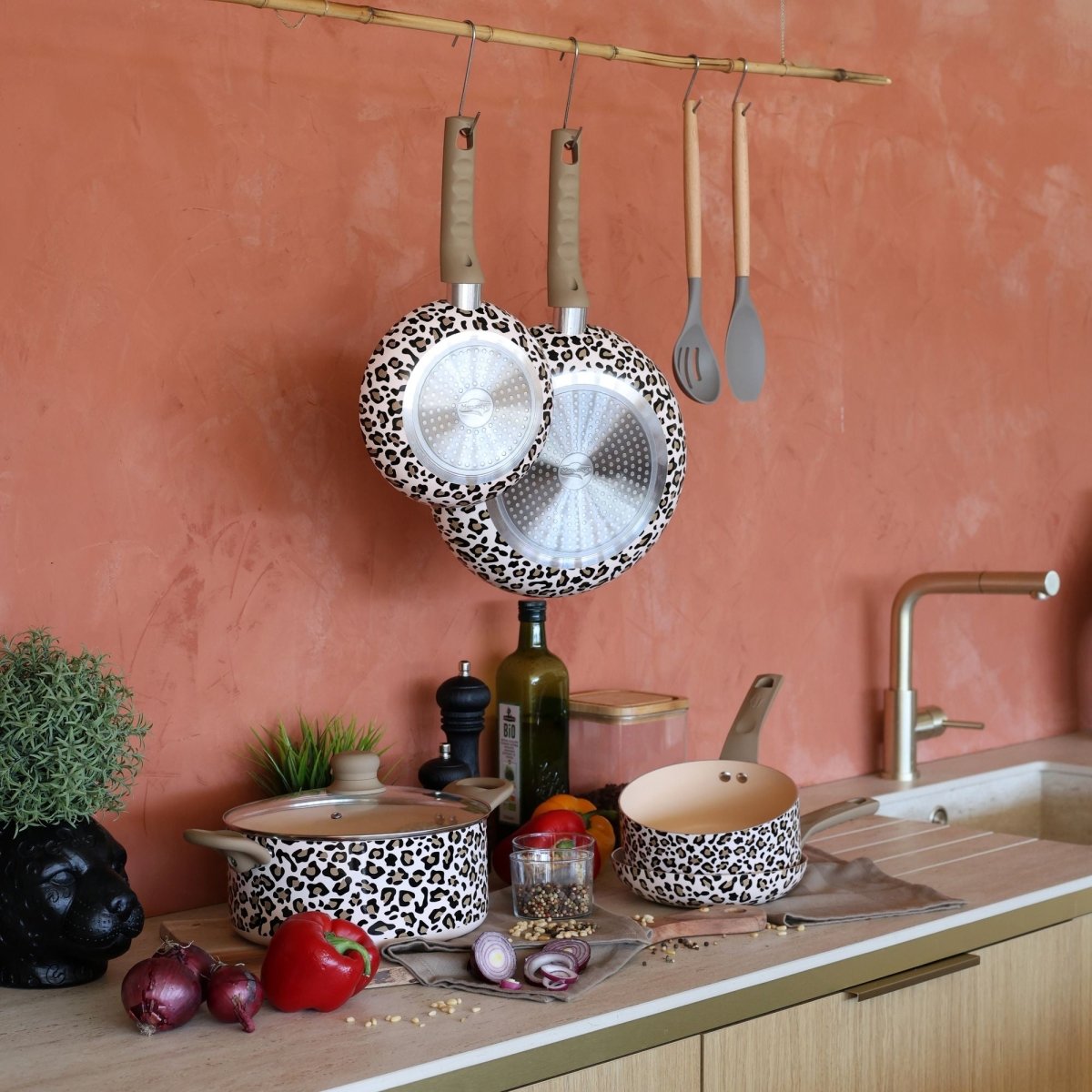 Set 5 pièces Léopard marron avec casseroles et poêles motif léopard, suspendu sur fond rose terracotta avec ustensiles