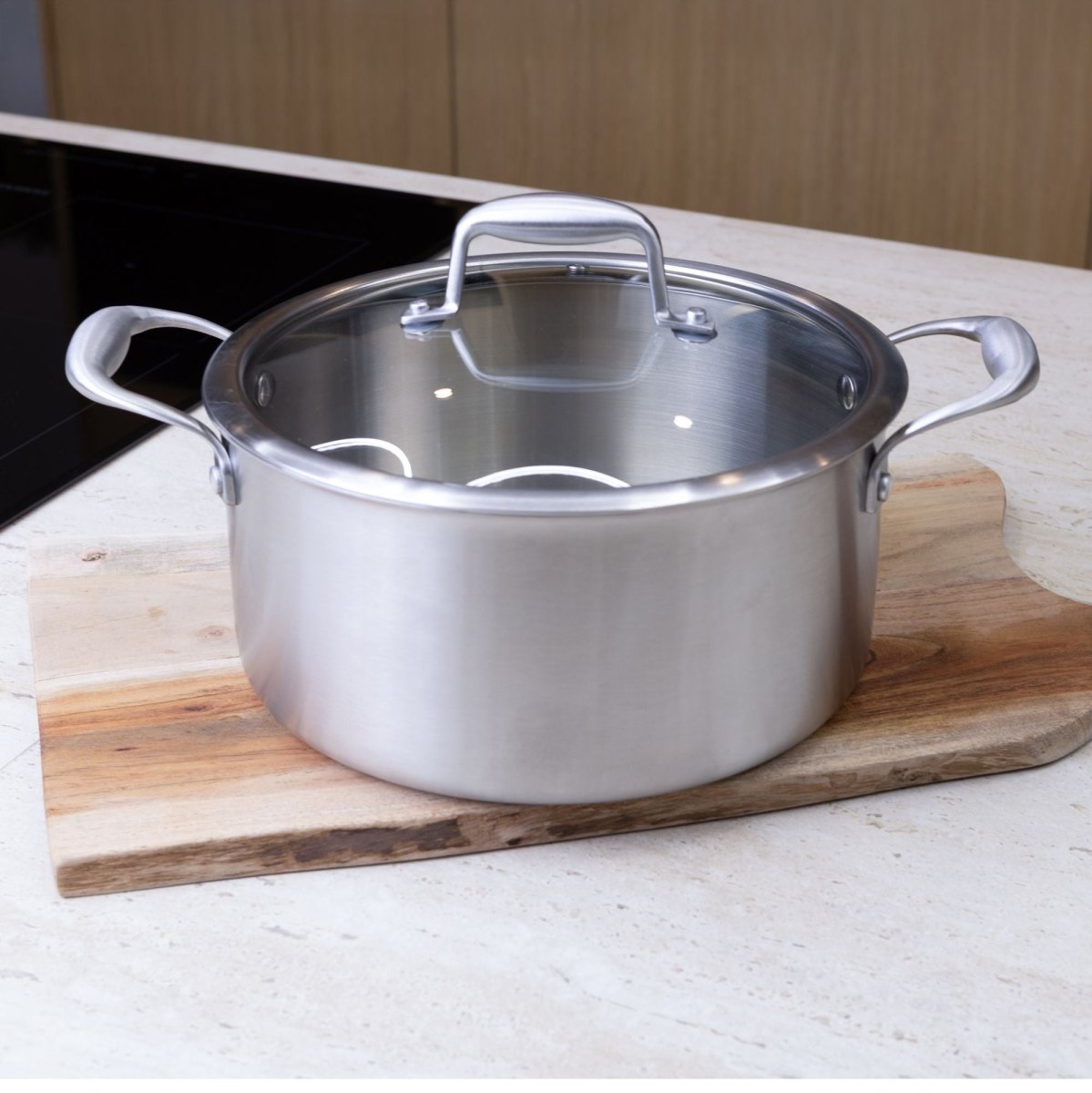 Casserole Trinox en acier inoxydable avec couvercle en verre posée sur planche bois, vue détail latéral