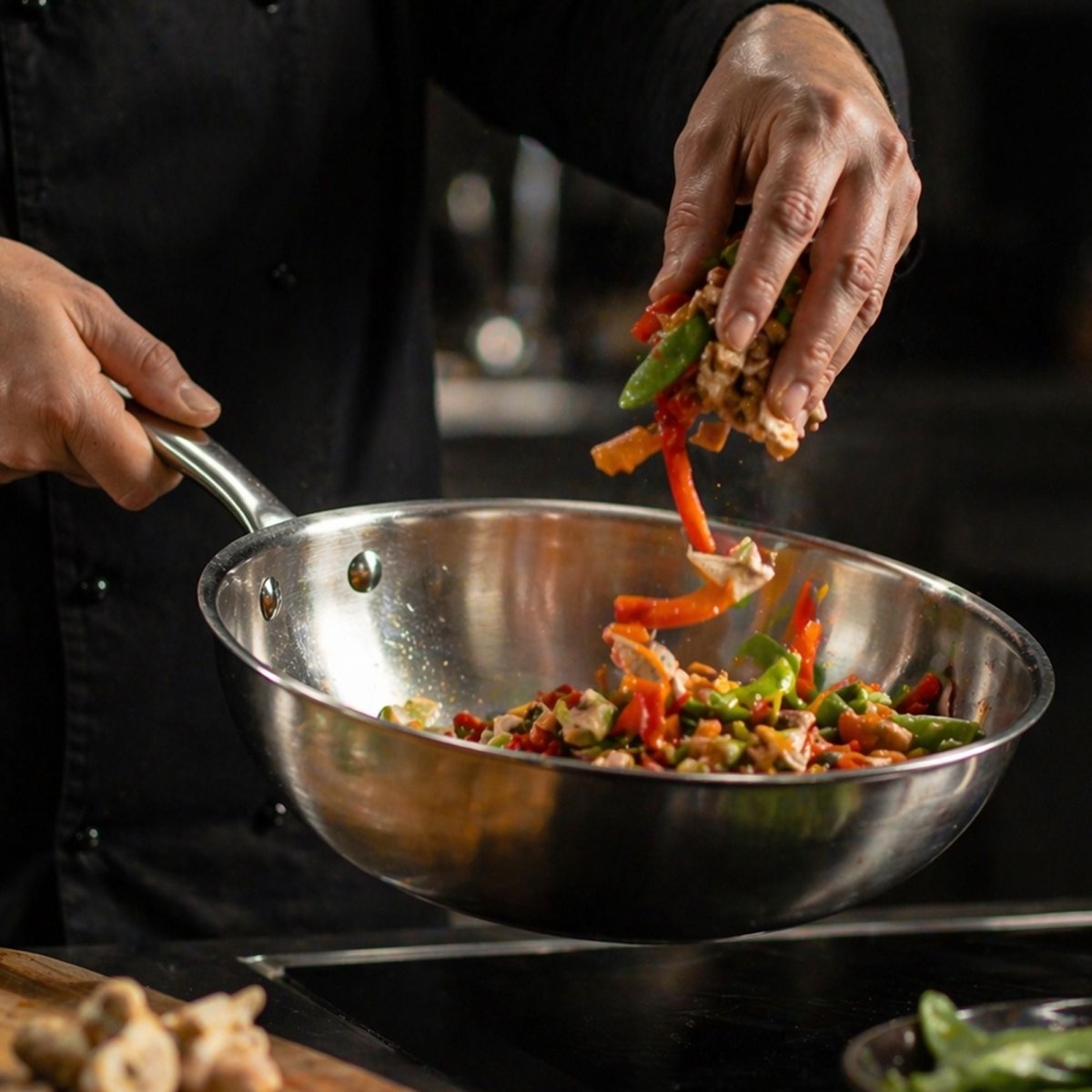 Chef cuisinant des légumes colorés dans un wok Triply 28cm en acier inoxydable sur plaque induction