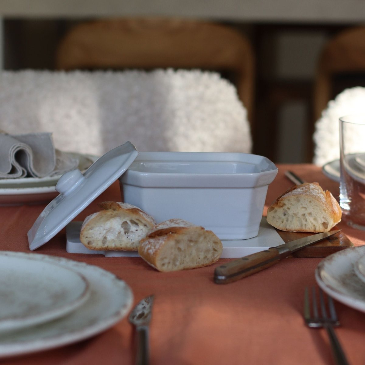 Terrine en grès blanc 400g avec couvercle posée sur table dressée, pain et couvert en arrière-plan