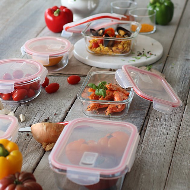 Boîtes hermétiques rectangulaires en verre avec couvercles à joint rouge, contenant divers aliments sur table en bois