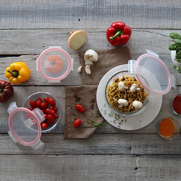 Boîtes hermétiques rondes avec couvercles roses contenant tomates cerises et pâtes aux champignons, mise en scène avec légumes sur table en bois
