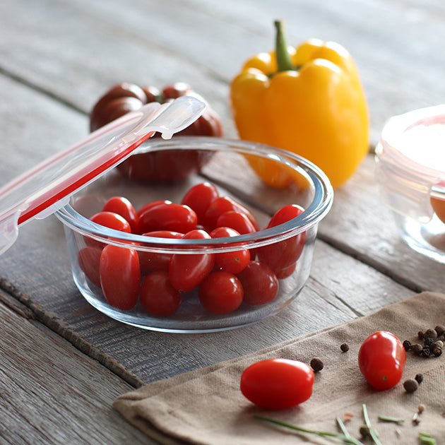 Boîte hermétique ronde en verre avec tomates cerises, couvercle ouvert et poivron jaune en arrière-plan