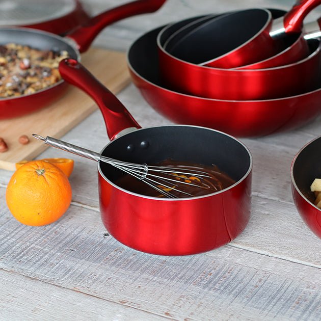Set de casseroles Cerise rouges en aluminium avec intérieur antiadhésif noir, disposées sur table avec fouet et orange