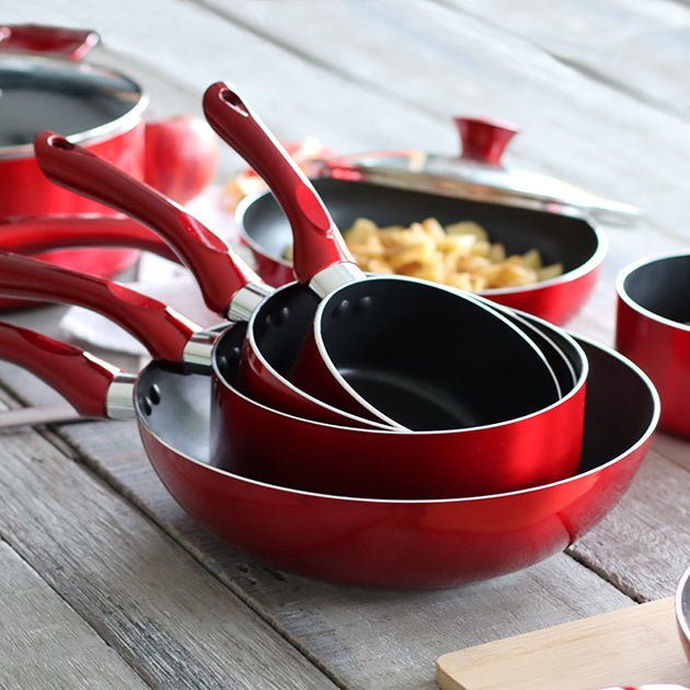 Ensemble de casseroles Cerise rouges en aluminium empilées avec ustensiles de cuisine assortis sur table en bois