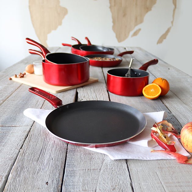 Collection de poêles et crêpières Cerise rouge en aluminium antiadhésif disposées sur table en bois rustique avec ingrédients