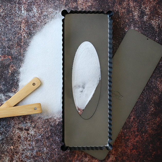 Moule à tarte rectangulaire Amandine 35 cm en acier carbone avec spatule bois sur plan de travail fariné