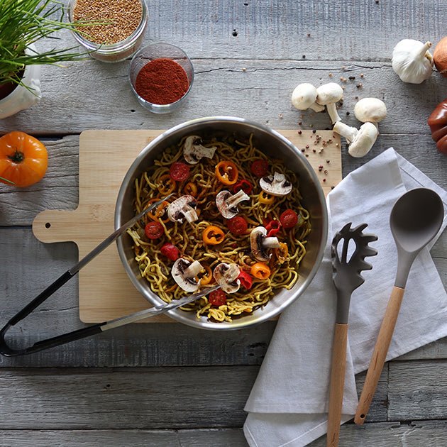 Wok Iris 28cm en acier inoxydable avec nouilles sautées, légumes et champignons, vue du dessus sur planche bois
